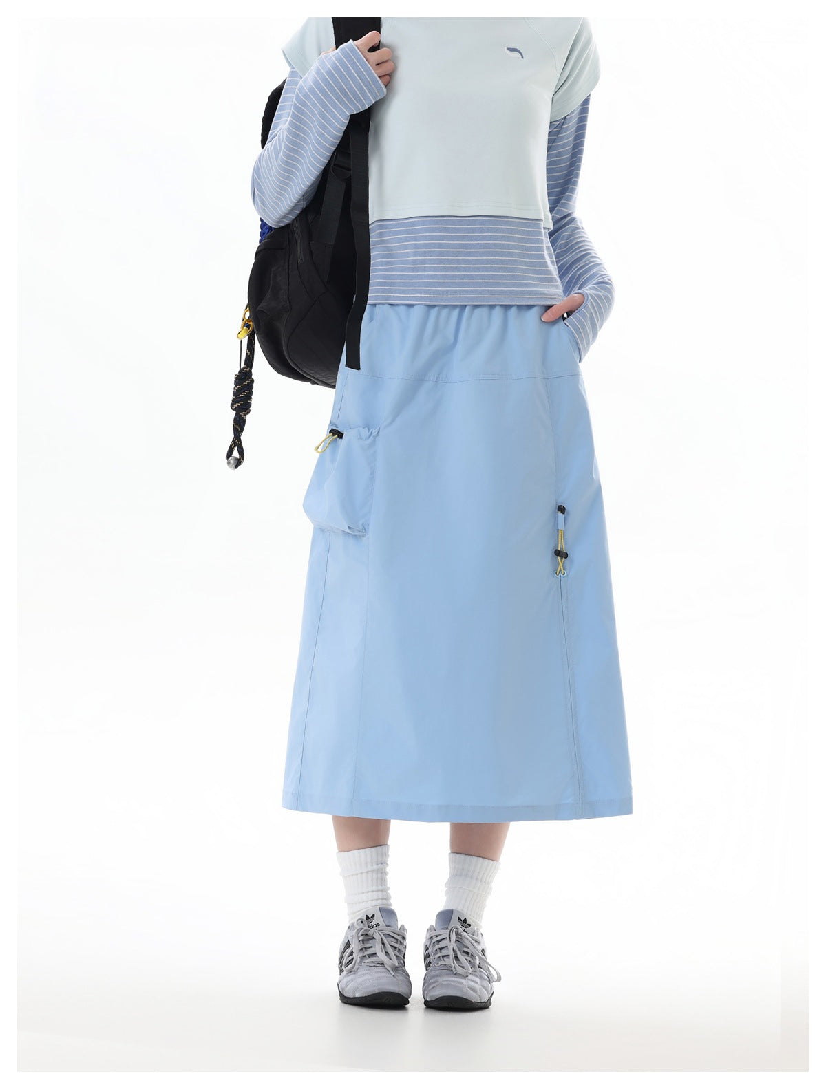 Front view of a model wearing a light blue midi skirt with a large pocket and yellow drawcord accents, paired with a