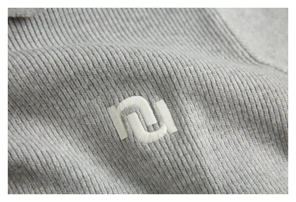 Close-up of a white embroidered emblem on a raised section of light gray ribbed knit fabric.