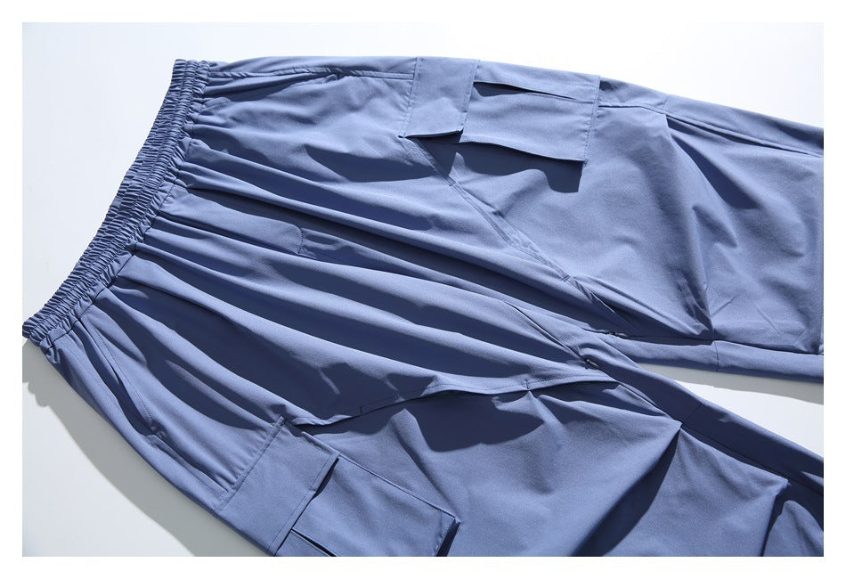 Close-up of slate blue pants laid diagonally, showing the elastic waistband and a flap cargo pocket.