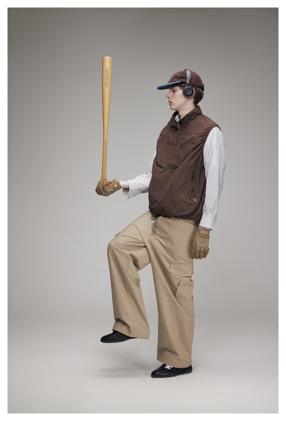 Full-length view of a model wearing a brown sleeveless zip vest, checked shirt, and loose khaki cargo pants.