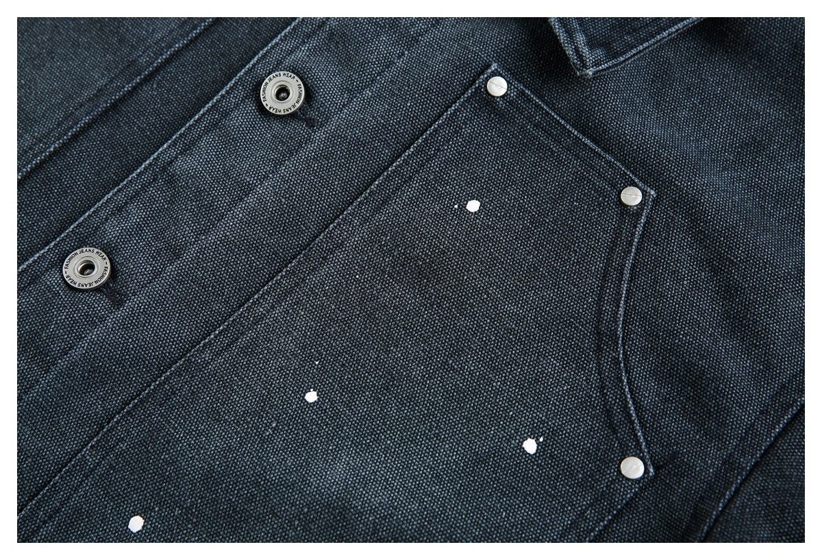 Close-up of dark indigo textured denim with a snap pocket, metal buttons and scattered white paint flecks.