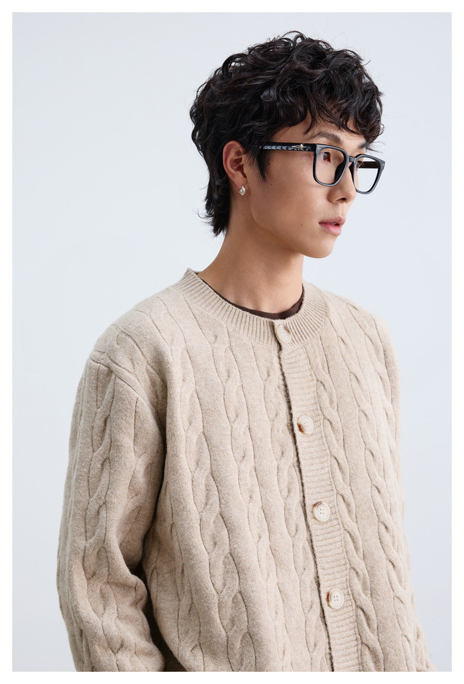 Close view of a model wearing a light beige cable-knit button cardigan, showing its collar and knit pattern.