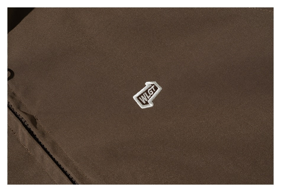 Close-up of a small white embroidered emblem on the chest of a brown jacket.