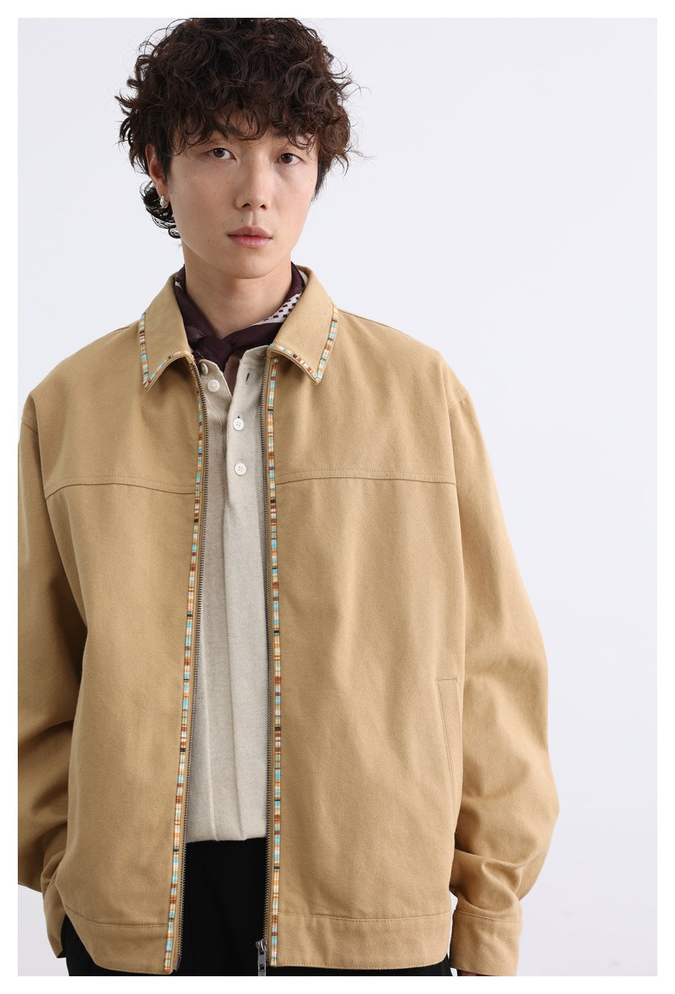 Close view of a model wearing a tan jacket with multicolor trim along the collar and open zipper, over a light polo.