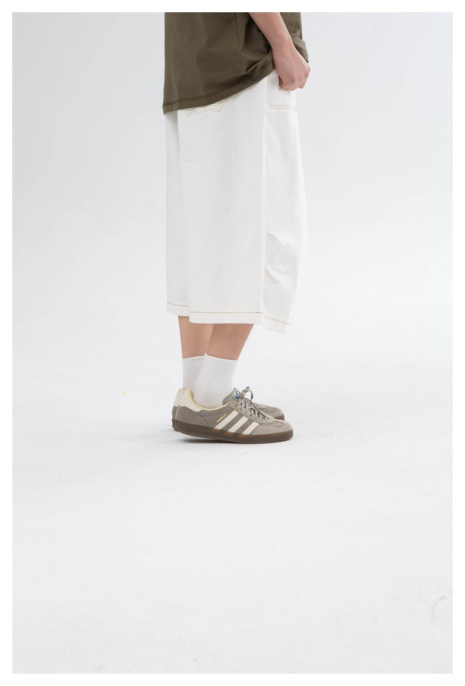 Side view of a model wearing wide white knee-length shorts with contrast stitching.