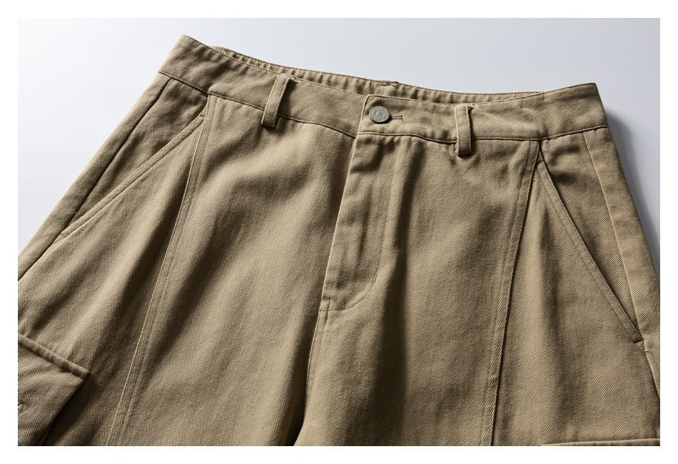 Cropped front view of khaki trousers showing the waistband, button, slanted pockets and pleats.