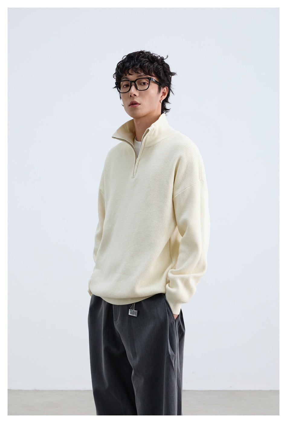 Model wearing an ivory quarter-zip pullover with the collar open and dark trousers.