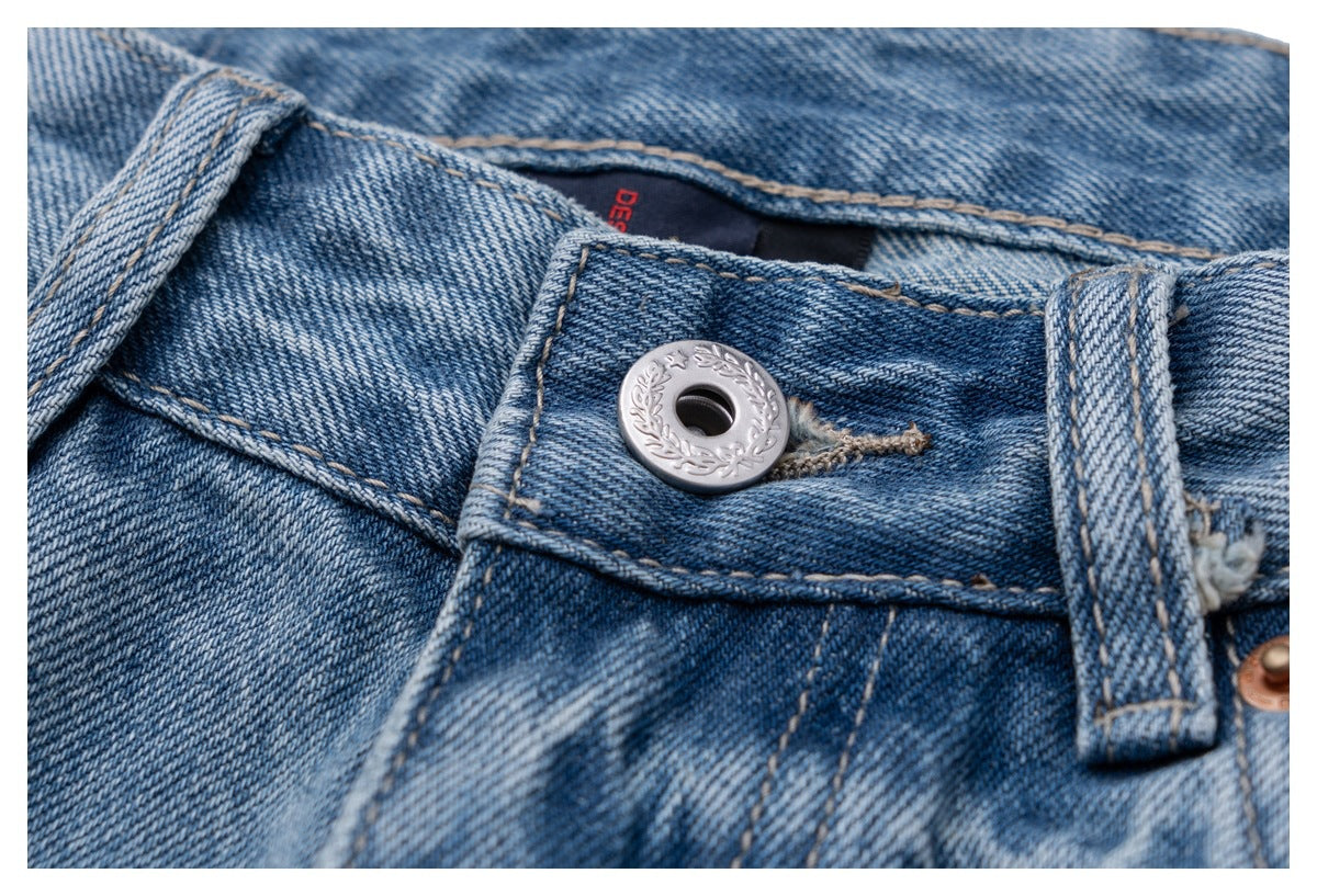 Close-up of light blue jeans waistband with a silver engraved button and belt loop.