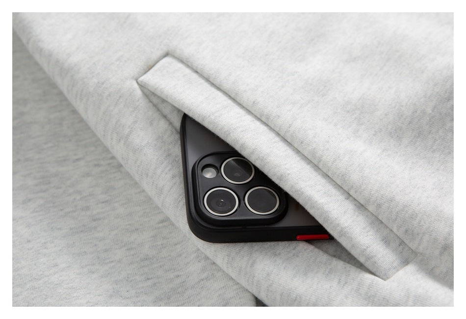 Close-up of a flap pocket holding a black smartphone on light gray heathered fabric.