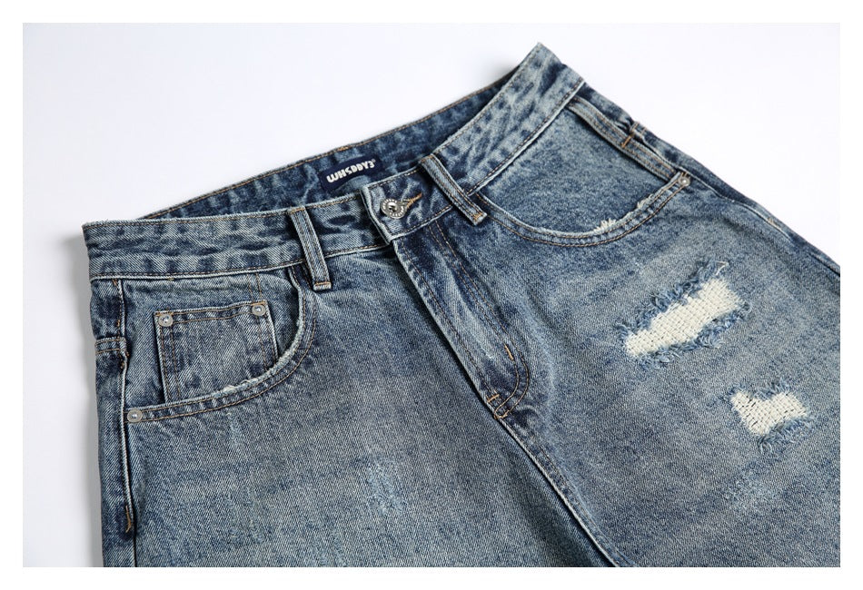 Cropped front view of blue acid-wash jeans with belt loops, pockets, a button closure, and distressed patches.