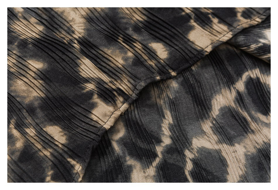 Close-up of a curved stitched seam across dark fabric with beige abstract print and fine pleats.