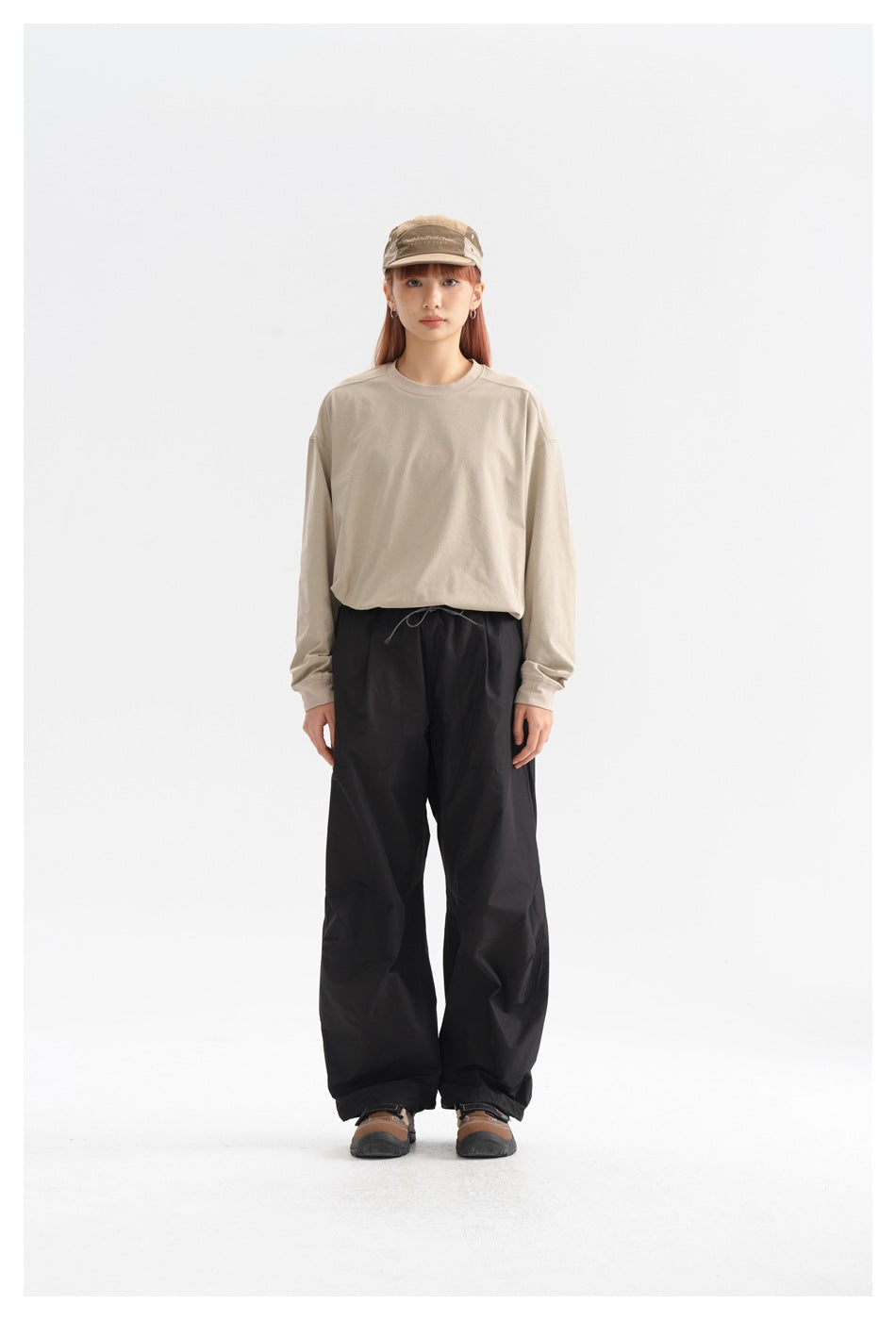 Model facing forward in loose black drawstring trousers and a beige long-sleeve shirt.