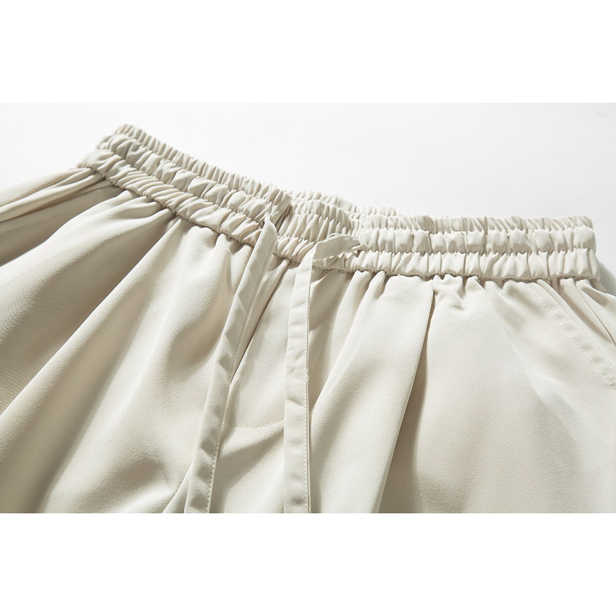 Close-up of cream trousers showing the gathered elastic waistband and front pleats.