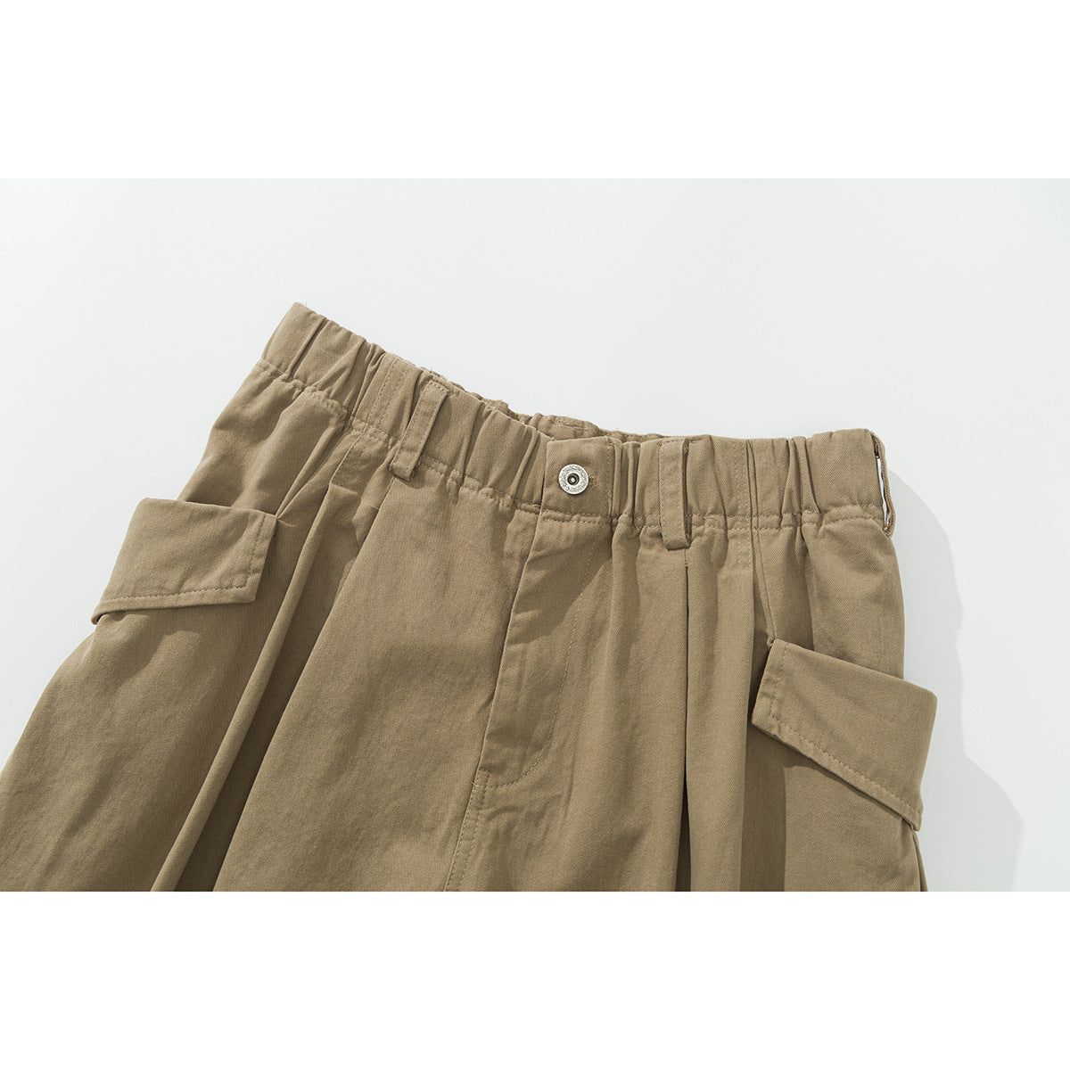 Close-up of khaki shorts showing the gathered waistband, button, belt loops and flap cargo pockets.