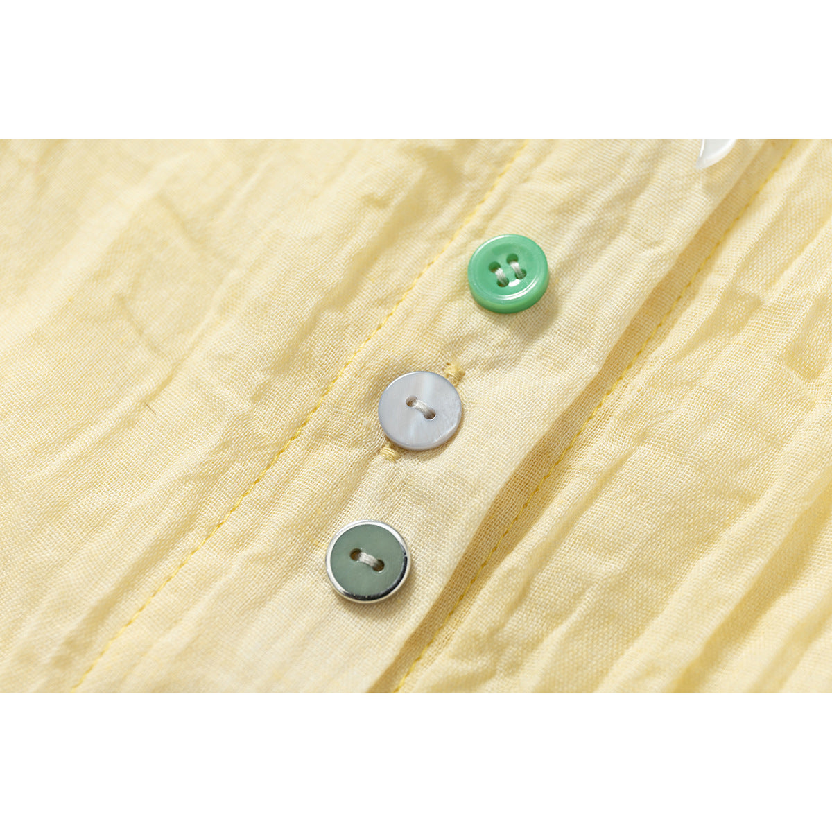 Close-up of three differently colored buttons on the pale yellow shirt placket.