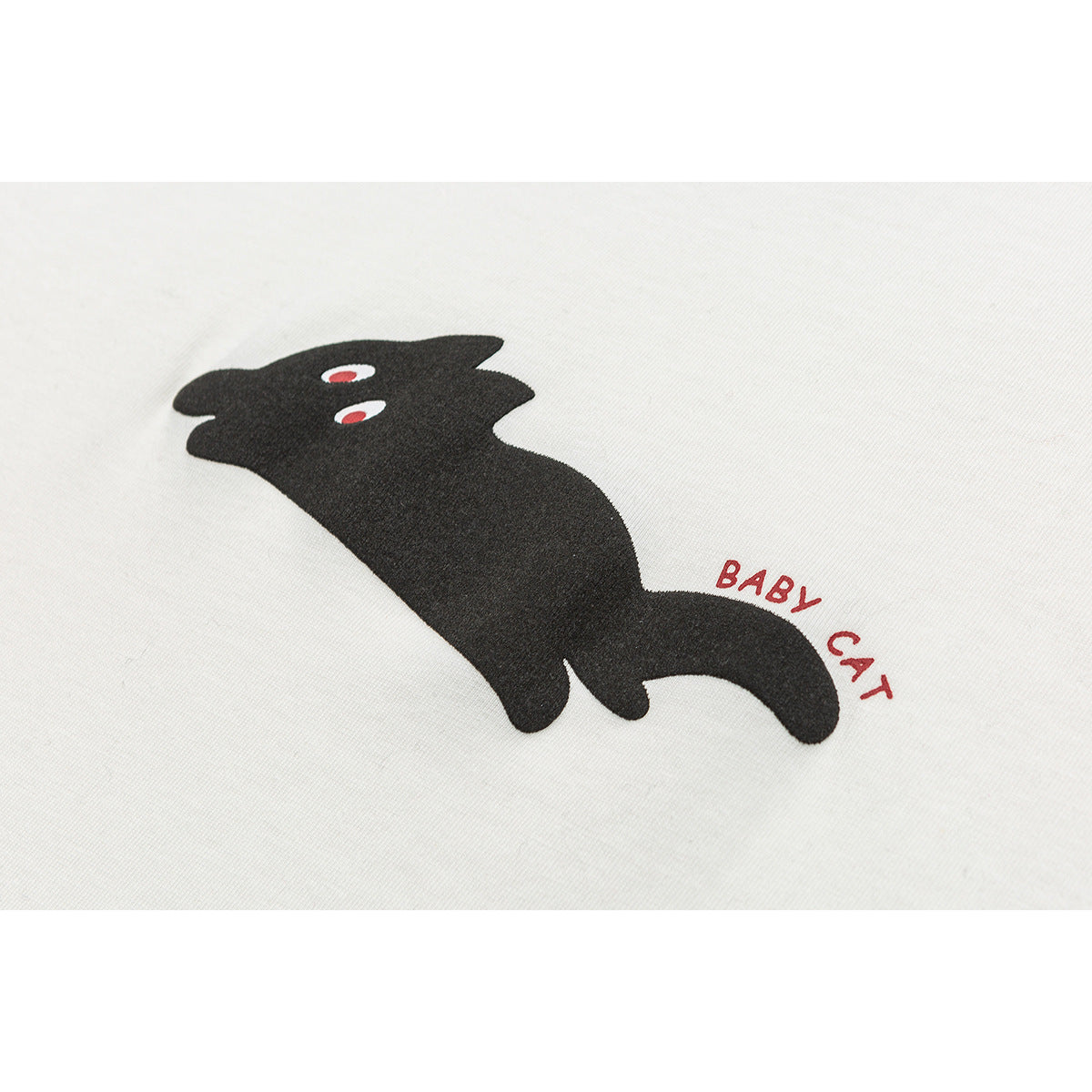 Close-up of a black cat graphic with red eyes and the words “BABY CAT” on ivory fabric.