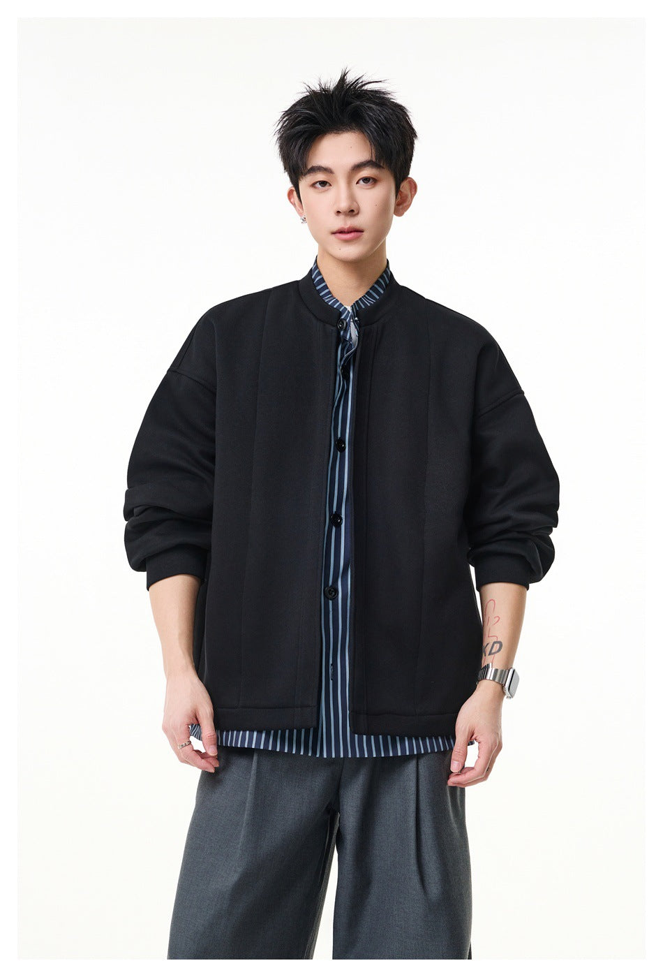 Model wearing a black jacket open over a navy and light blue striped buttoned shirt with gray trousers