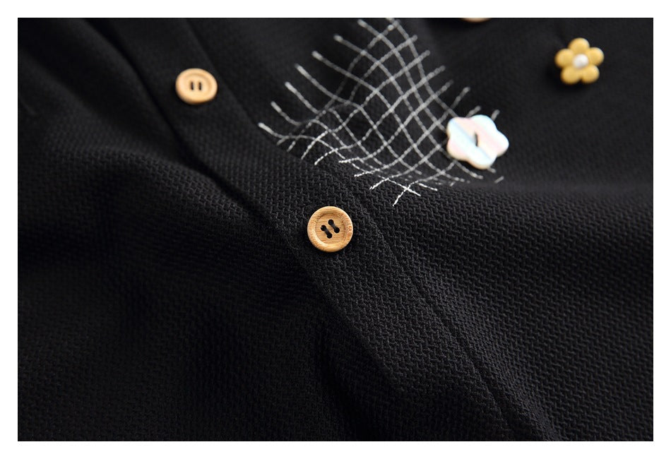 Close-up of a black garment with tan buttons, white crosshatch stitching, and decorative flower buttons.