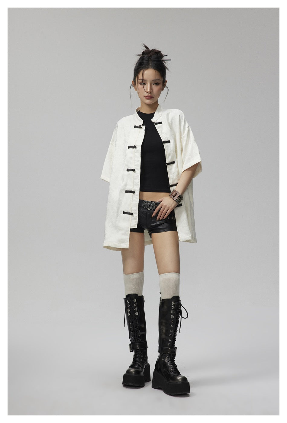 Model in an off-white knot-button short-sleeve shirt worn open over a black top, with black shorts and lace-up boots