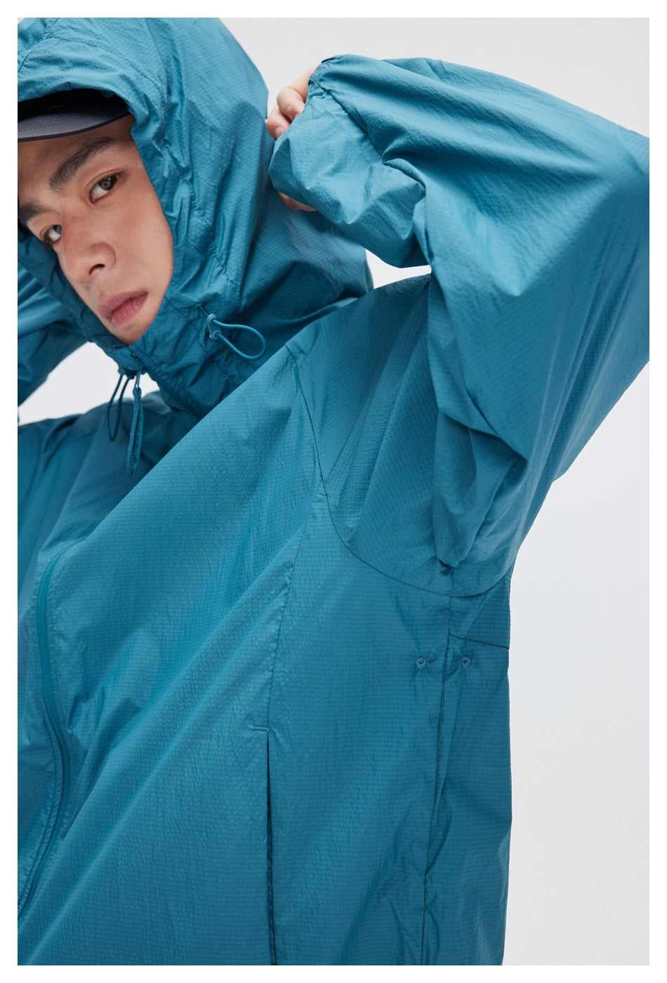 Close-up of a teal hooded jacket showing its fabric texture, hood drawcord, and sleeve construction.