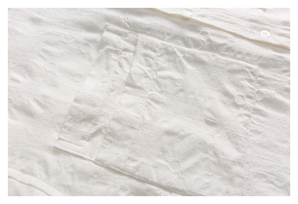 Close-up of a white shirt’s textured fabric and rectangular chest pocket.