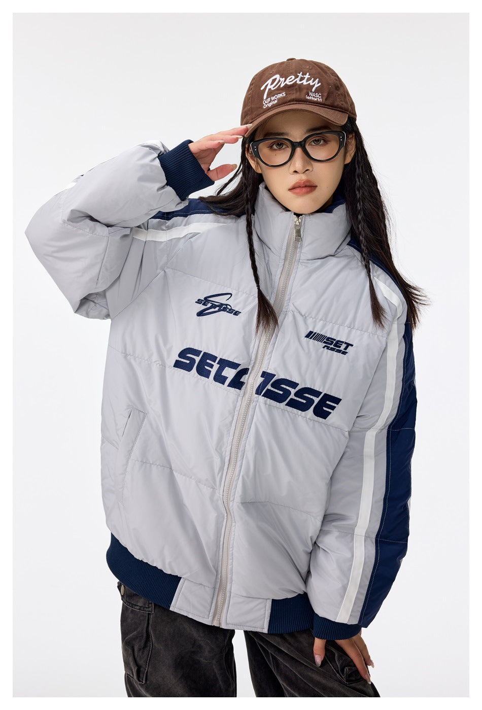Model wearing a light gray padded zip jacket with navy panels, white sleeve stripes, ribbed cuffs and dark chest lettering.