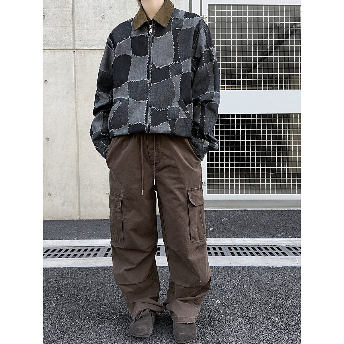 Cropped model wearing a charcoal patchwork zip jacket with a brown collar and loose brown cargo pants.