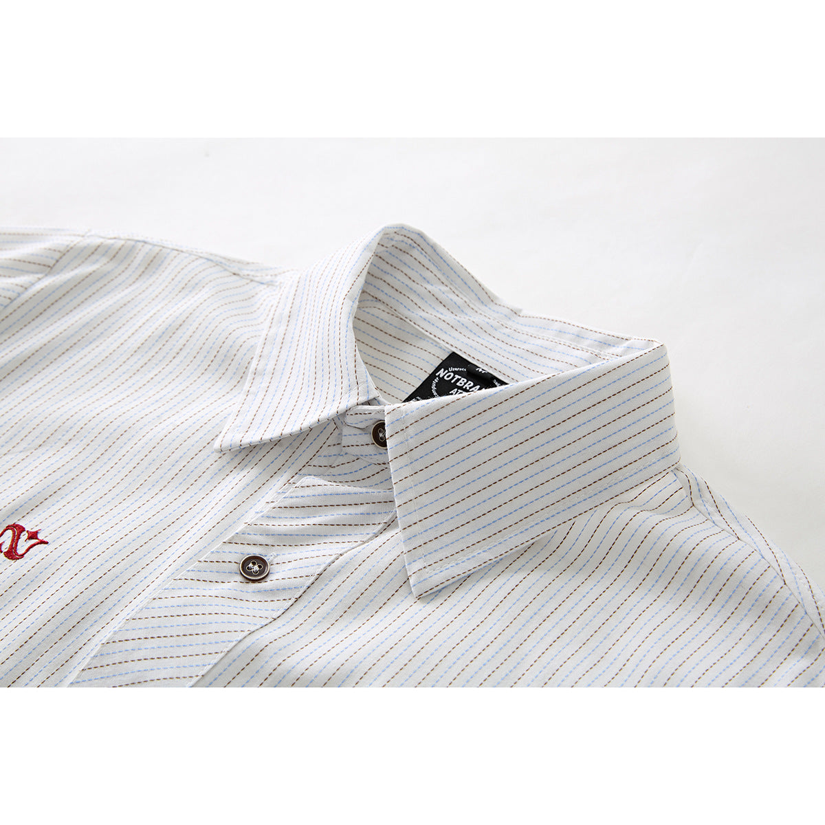 Close-up of a white shirt collar and button with fine blue and brown stripes and a black neck label.