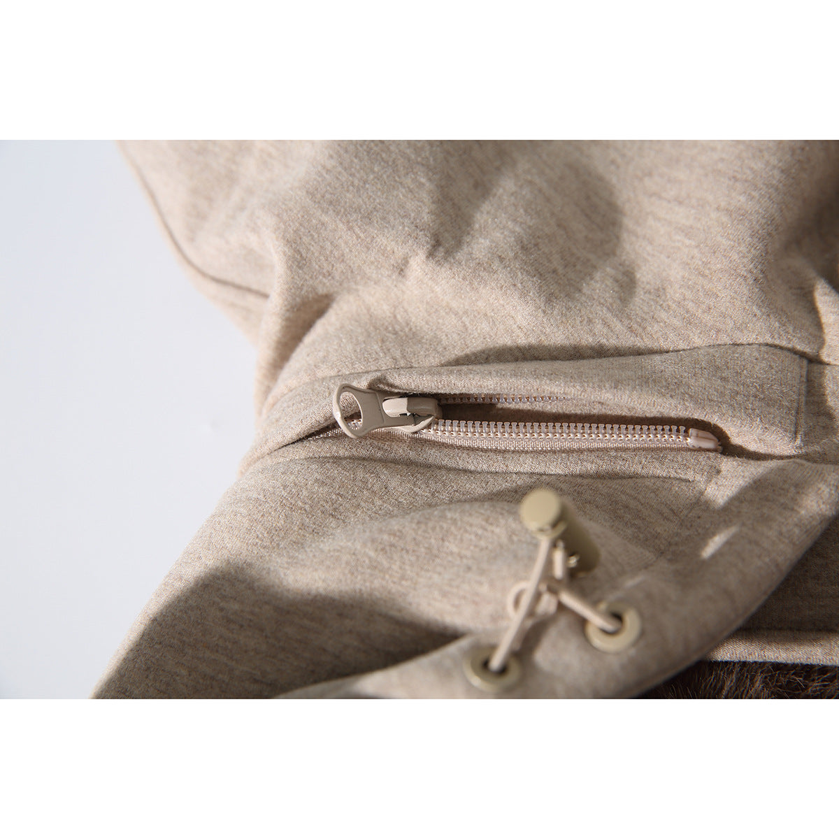 Close-up of a beige vest's hood drawcord and concealed zipper detail.
