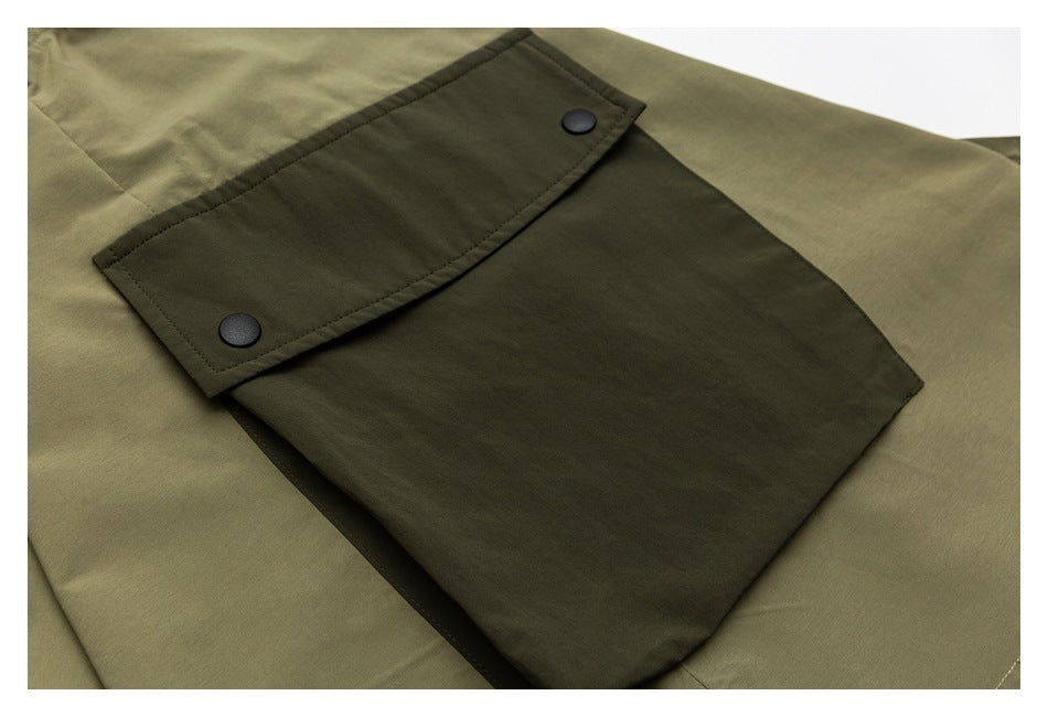 Close-up of a dark olive flap pocket with two black snaps on a lighter olive garment.