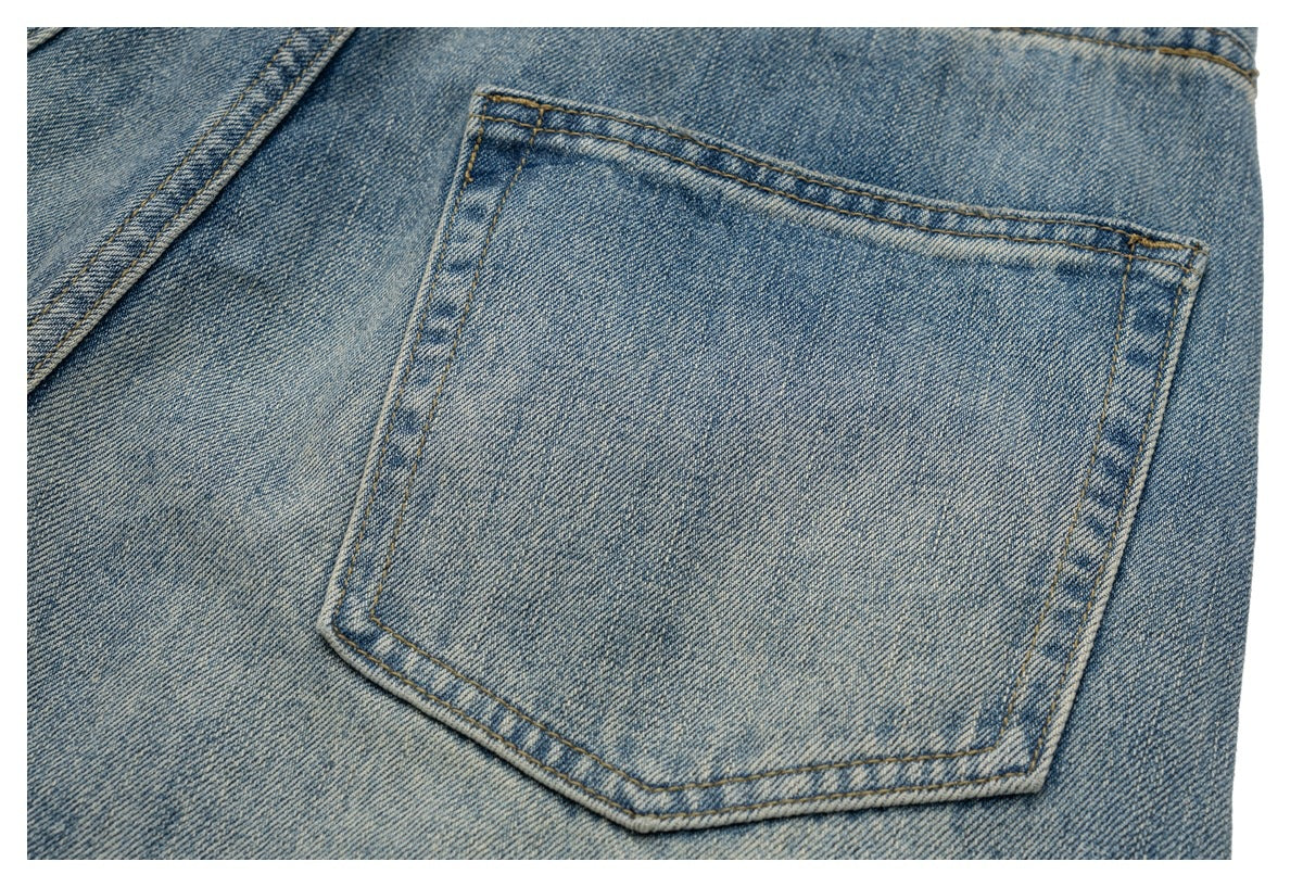Close-up of a large back pocket on light-wash blue denim jeans with golden stitching.