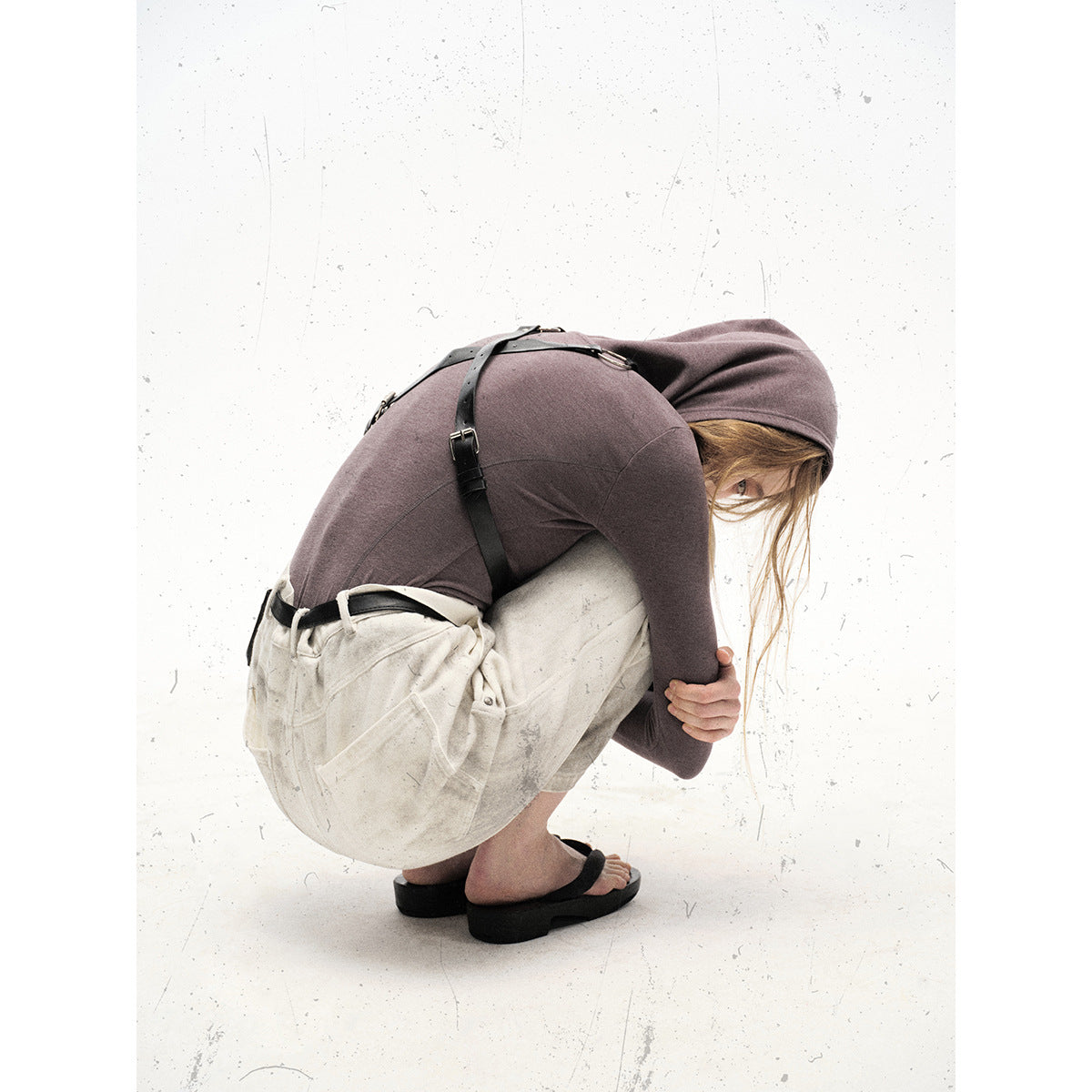 Model crouching in off-white, mottled wide-leg utility pants with large pockets and a mauve hooded top.