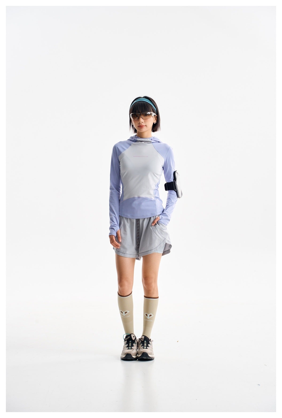 Model wearing a light blue and pale gray hooded long-sleeve top with gray running shorts, shown full length.