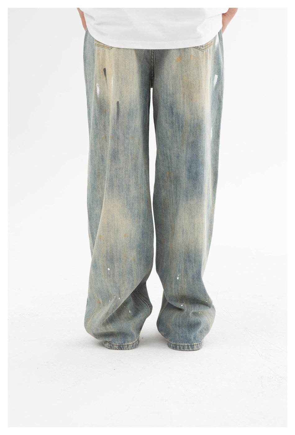 Rear view of wide faded blue jeans with scattered distressed paint-like marks, worn with a white shirt.