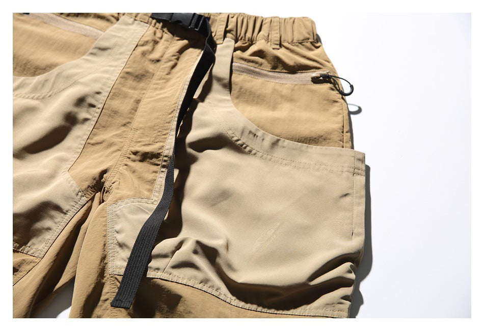 Close-up of tan shorts with an elastic waistband, zip pocket, black strap, and large side pocket.