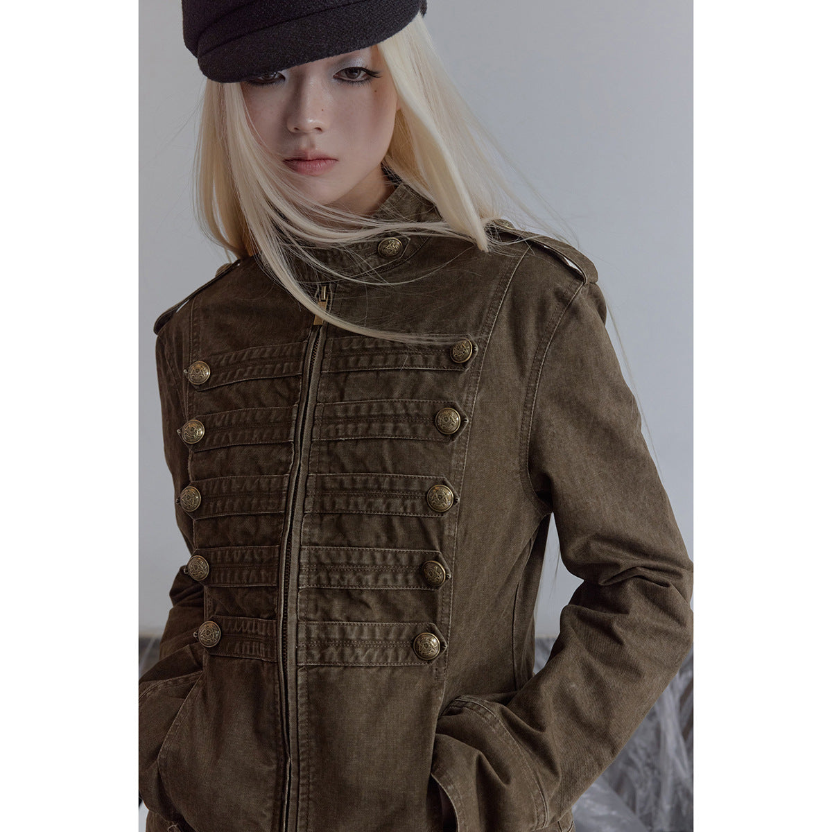 Close view of a model wearing an olive-brown jacket with a stand collar and rows of decorative brass buttons.