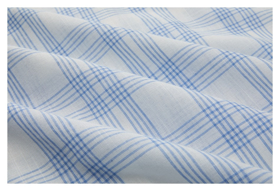 Close-up of white fabric with a light blue plaid pattern, draped in soft folds.