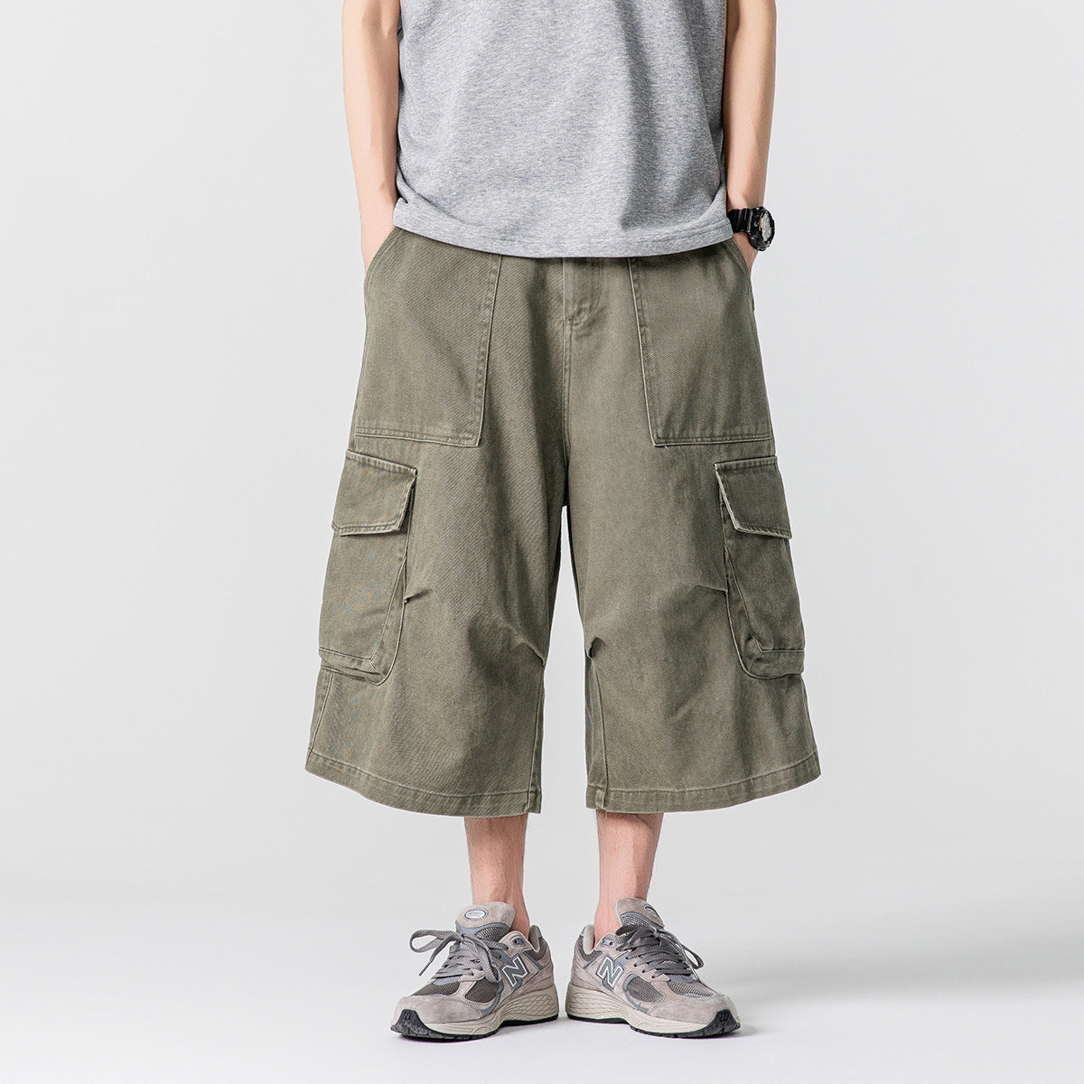 Front view of a model wearing loose olive cargo shorts with large front and flap side pockets.