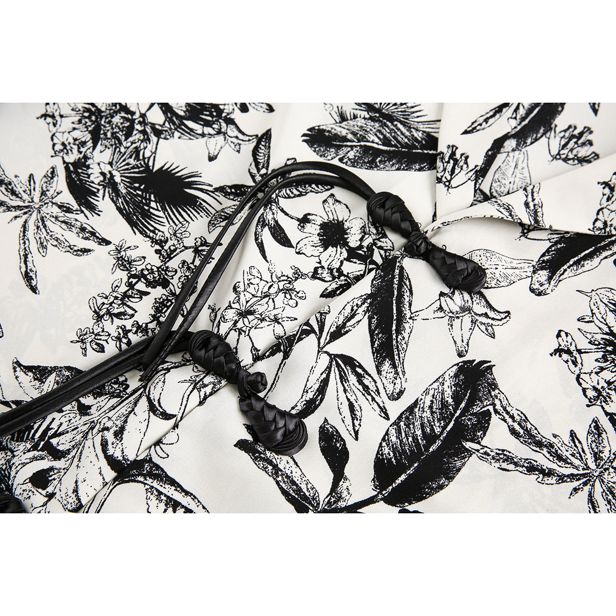 Close-up of an ivory garment with a black botanical print and black braided cord ties with knotted ends.