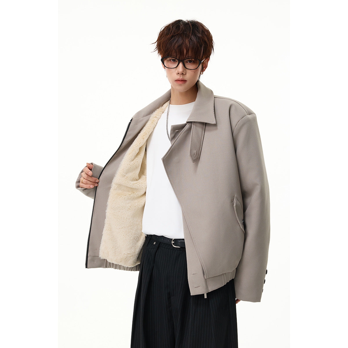 Model wearing an open taupe jacket with cream sherpa lining, white shirt, and black pinstripe trousers.