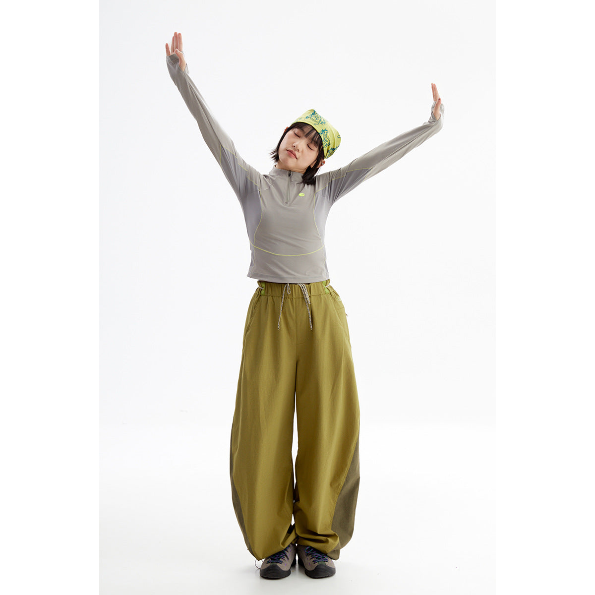 Full-length model in a gray quarter-zip top with lime piping and loose olive pants, arms raised.