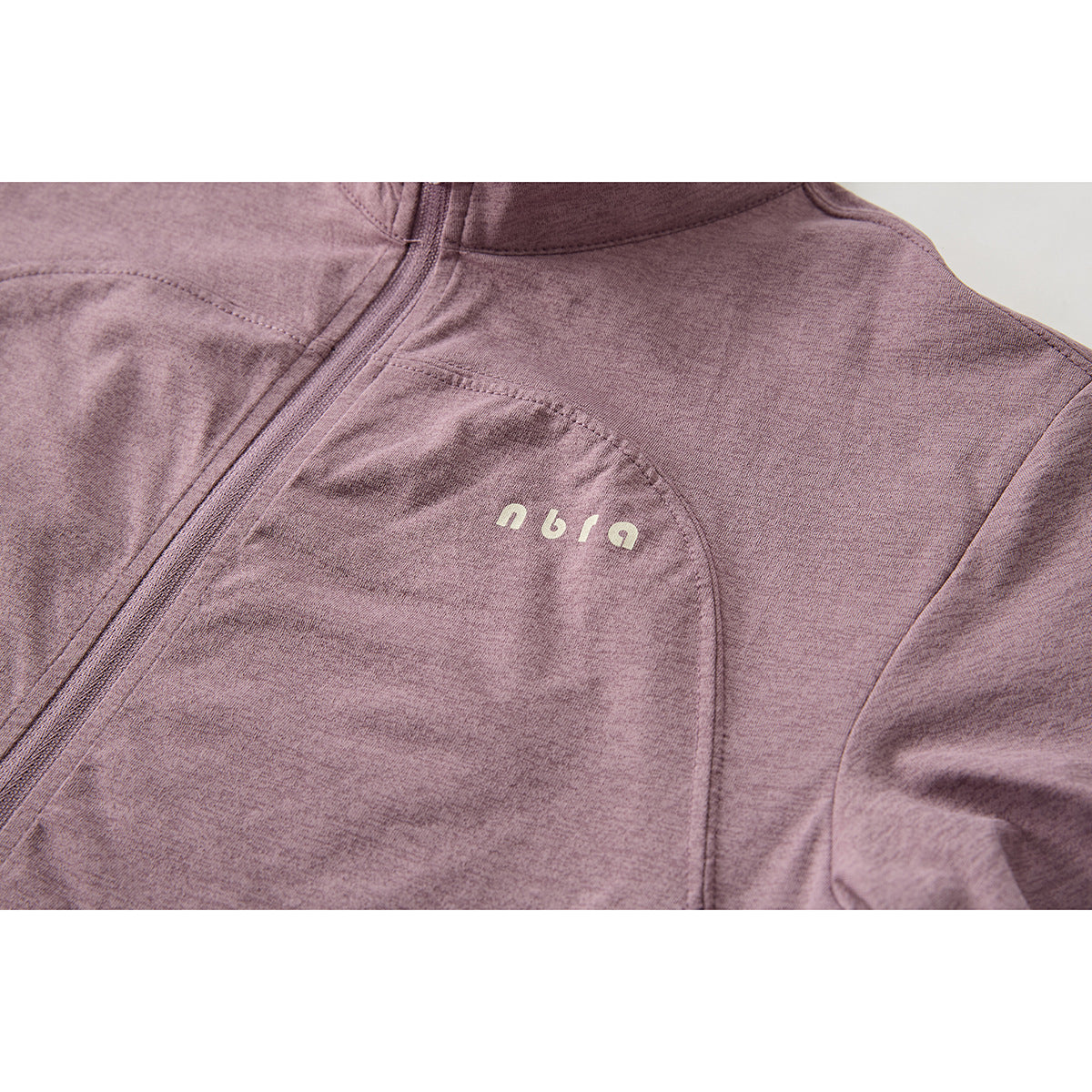Close-up of a mauve zip top showing curved chest seams and a small pale logo on the chest.