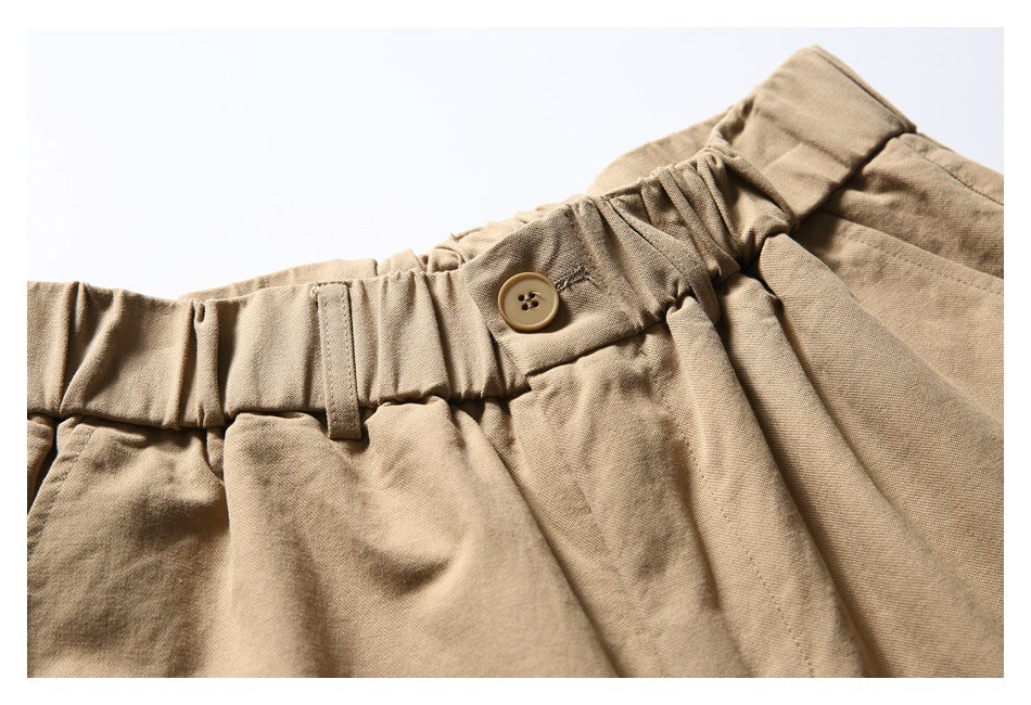 Close-up of the tan shorts' gathered waistband, belt loop, and button closure.