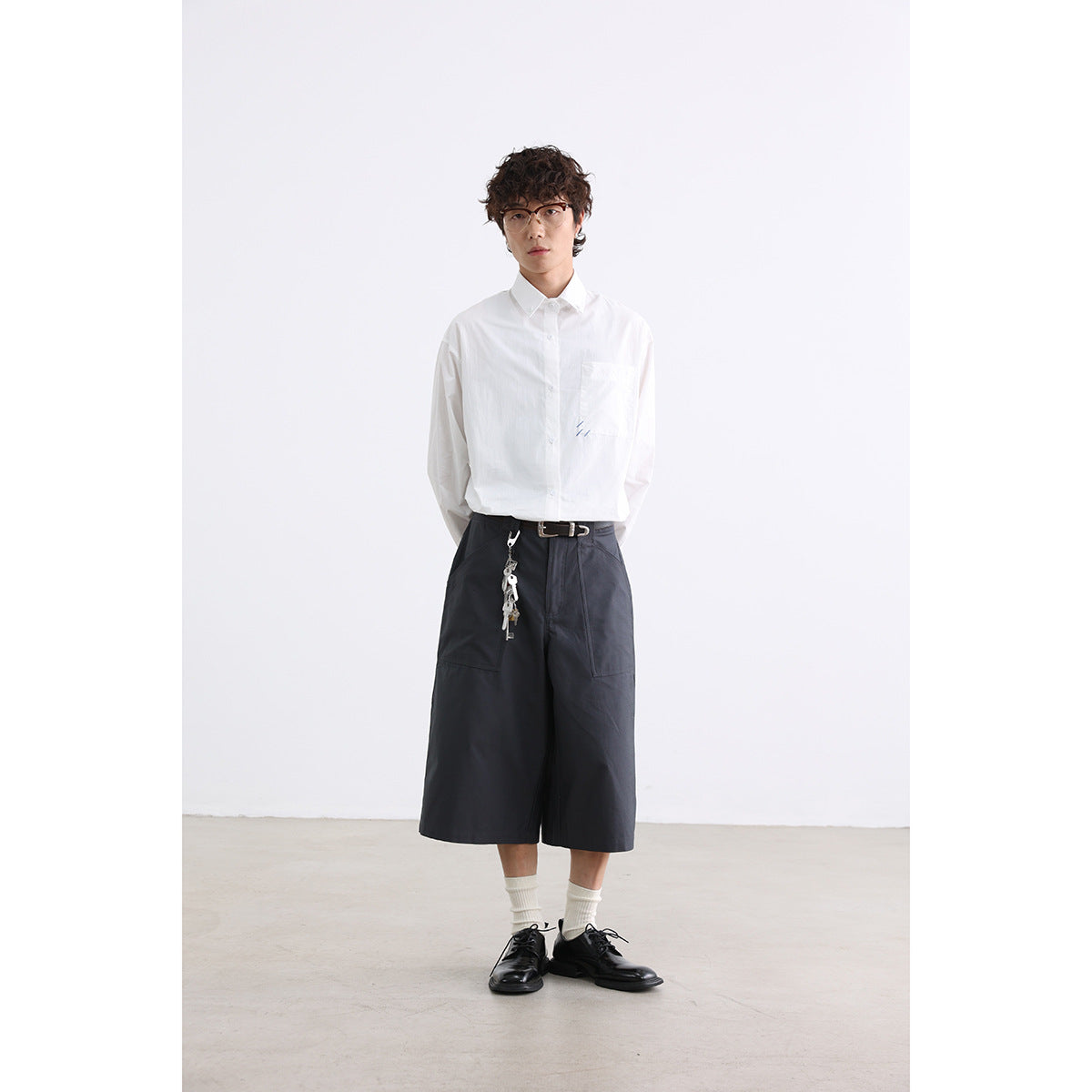 Full-length model wearing a white button-down shirt, charcoal wide-leg shorts, and black shoes.