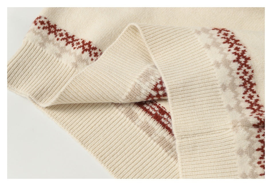 Close-up of a cream sweater sleeve and ribbed cuff with a red and gray patterned band.