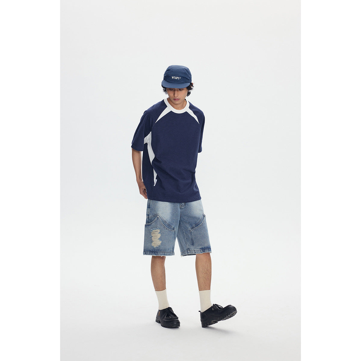 Model wearing a navy and white raglan T-shirt and distressed light-wash denim shorts, viewed from the front.