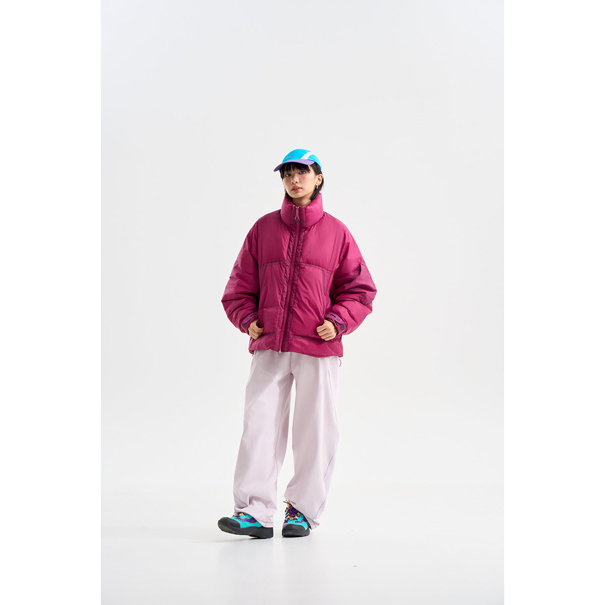 Model wearing a magenta oversized puffer jacket with a high collar and loose pale trousers.