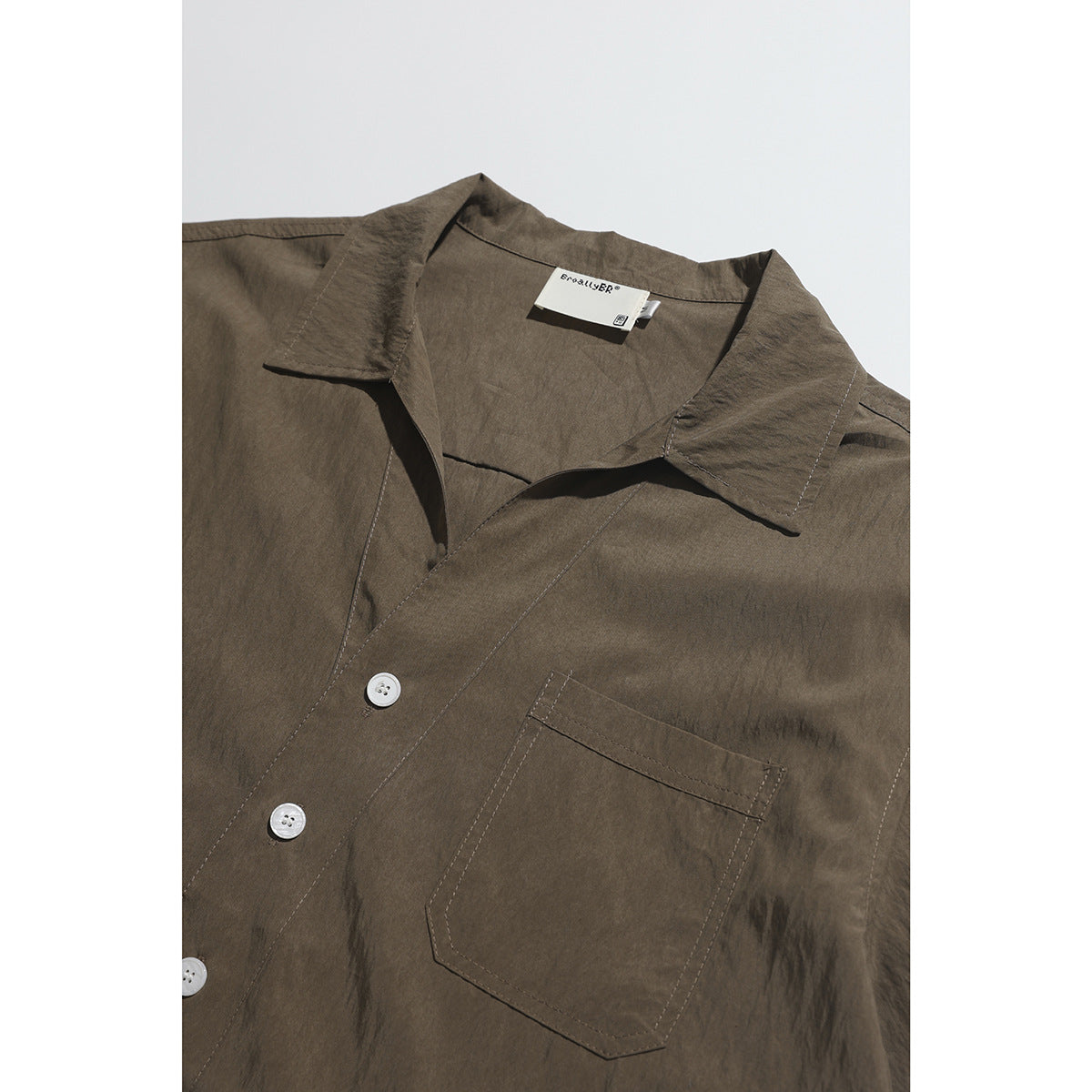 Close-up of a brown short-sleeve shirt showing its open collar, white buttons, chest pocket, and neck label.