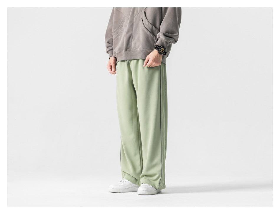 Three-quarter view of a model wearing pale sage-green wide-leg pants with a gray hoodie and white sneakers.