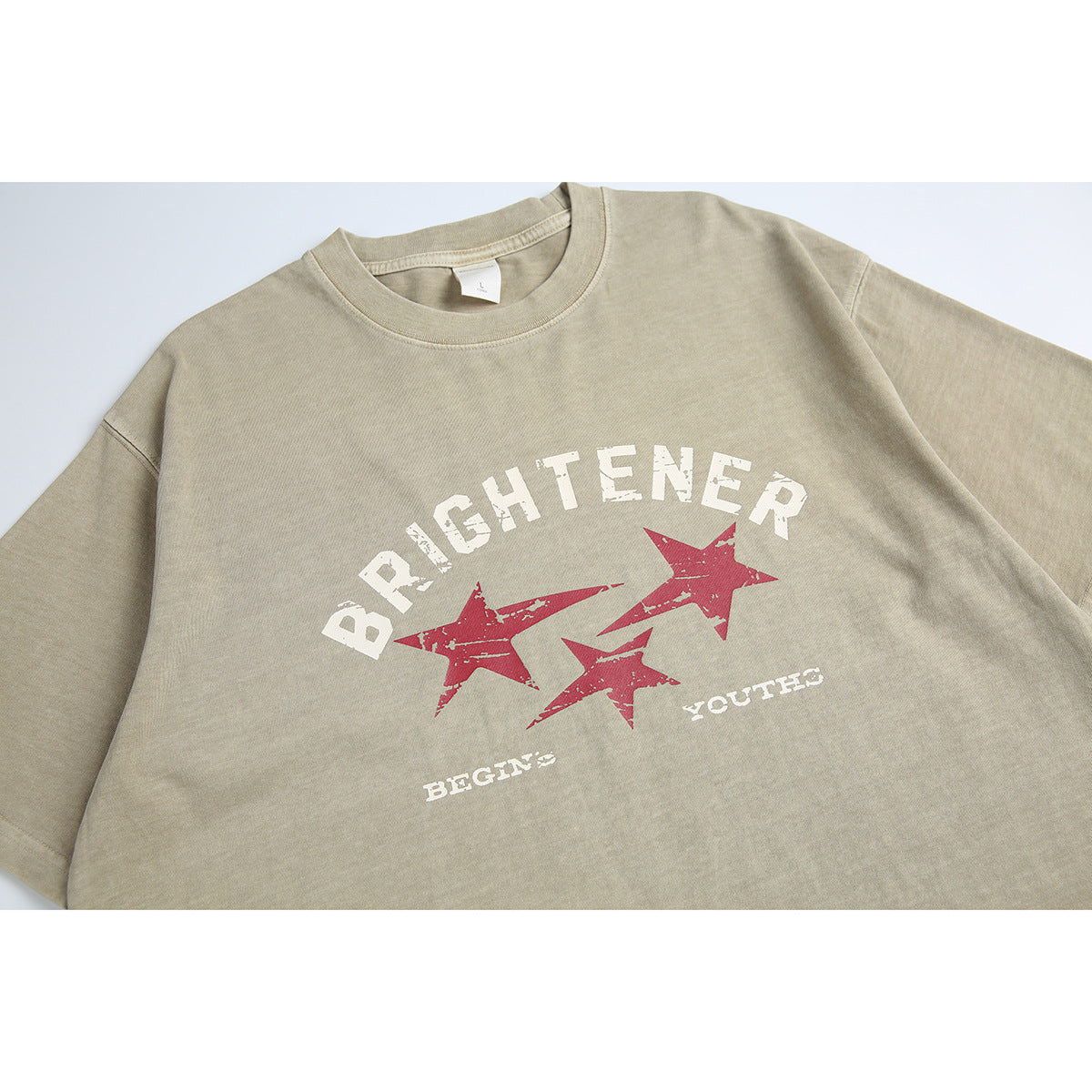 Close view of a beige crew-neck T-shirt front with distressed white lettering and three red stars.